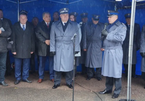Grupa policjantów i urzędników w długich płaszczach stoi pod niebieskim namiotem podczas otwarcia Posterunku Policji w Staroźrebach.