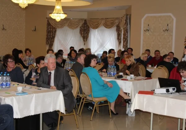 Uczestnicy IV Konferencji Partnerstwa Lokalnego powiatu płockiego siedzą przy stołach w sali konferencyjnej podczas prezentacji, a osoba z mikrofonem prowadzi wystąpienie po prawej stronie.