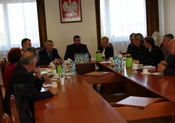 Grupa urzędników i gości siedzi przy długim drewnianym stole w sali konferencyjnej podczas obchodów 100-lecia Odzyskania Niepodległości w Powiecie Płockim, na ścianie widnieje godło Polski.