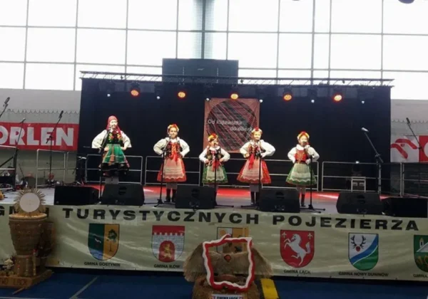 Pięć tancerek w tradycyjnych, kolorowych strojach ludowych tańczy na scenie podczas 12. Festiwalu Folkloru i Kultury Ziemi Kujawskiej i Mazowieckiej „Od Kujawiaka do Oberka”.