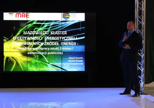 Mężczyzna w garniturze przemawia na scenie obok dużego, kolorowego ekranu prezentacyjnego podczas I Mazowieckiego Forum Energii Odnawialnych.