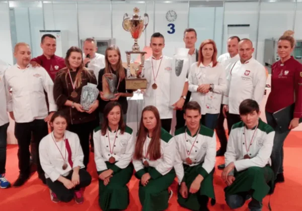 Zawodnicy i trenerzy w białych strojach z medalami stoją wokół dużego pucharu podczas Pucharu Polski Juniorów w Carvingu.