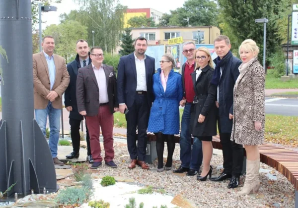 Grupa osób w eleganckich ubraniach stoi obok instalacji energetycznego drzewka OZE podczas uroczystego oddania do użytku.