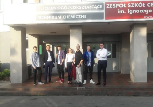 Grupa uczniów stoi przed wejściem do Zespołu Szkół w Gąbinie, pod szyldem widoczne są napisy o liceum ogólnokształcącym i technikum chemicznym.