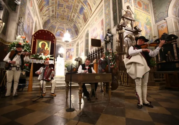 Zespół muzyków w tradycyjnych polskich strojach ludowych gra w barwnym kościele z ikonami i freskami podczas Dnia Papieskiego w Płocku.