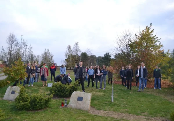 Grupa młodzieży z Bergerowej stoi na trawniku w parku jesienią, otoczona drzewami i kamiennymi tablicami, przygotowując realizację dwóch nowych projektów.
