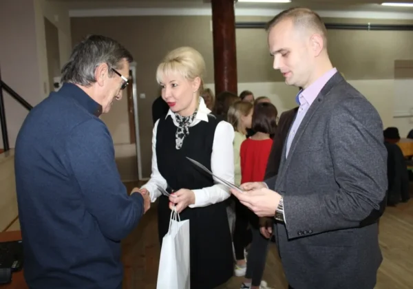 Trzy osoby w eleganckich strojach rozmawiają i wręczają dokumenty podczas spotkania podsumowującego projekt „Zachwyć się moim miejscem na Ziemi”.