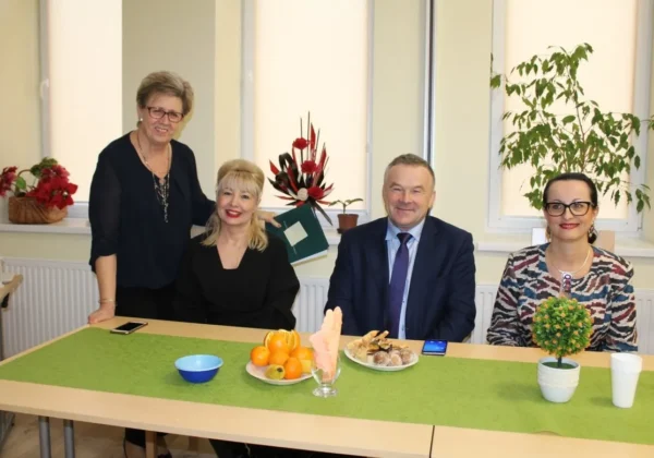 Cztery osoby uczestniczące w XI Przeglądzie Twórczości Literackiej Emerytów, Rencistów i Inwalidów „Trening Pamięci” siedzą i stoją przy stole z owocami, ciastkami i napojami, a w tle znajdują się rośliny i okna.