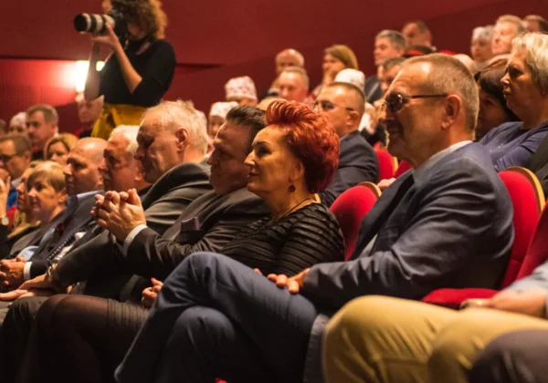 Widownia w sali teatralnej podczas gali wręczania nagród Marszałka; na pierwszym planie kobieta z czerwonymi włosami siedzi w czarnym stroju, wśród innych uczestników, a w tle stoi fotograf.