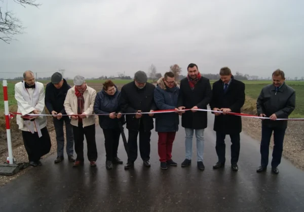 Grupa osób podczas uroczystego otwarcia stoi na nowo wyasfaltowanej drodze powiatowej Rębowo-Orszymowa i przecina wstęgę.