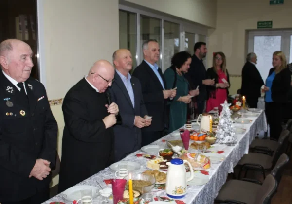 Uczestnicy Wigilii Polskiego Związku Emerytów, Rencistów i Inwalidów Koła Terenowego w Bielsku stoją przy długim, suto zastawionym stole z potrawami i świątecznymi dekoracjami.