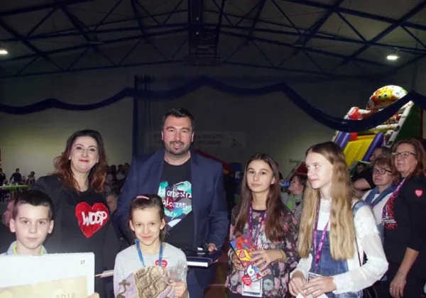 Grupa dorosłych i dzieci w hali sportowej podczas WOŚP w powiecie płockim, trzymająca upominki.