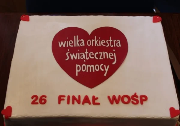 Tort ozdobiony dużym czerwonym sercem z napisem „wielka orkiestra świątecznej pomocy” oraz napisem „26 finał WOŚP”.