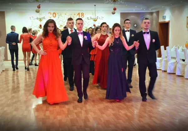 Uczestnicy studniówki w powiecie płockim tańczą w parze w eleganckich balowych kreacjach na tle dekorowanej sali z napisem 2018.