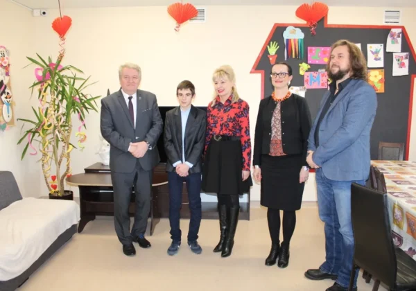 Wychowanek Placówki Opiekuńczo-Wychowawczej w Wyszogrodzie stoi z czterema dorosłymi w dekorowanym wnętrzu podczas wręczania wyróżnienia Wojewody Mazowieckiego w konkursie na kartkę świąteczną.