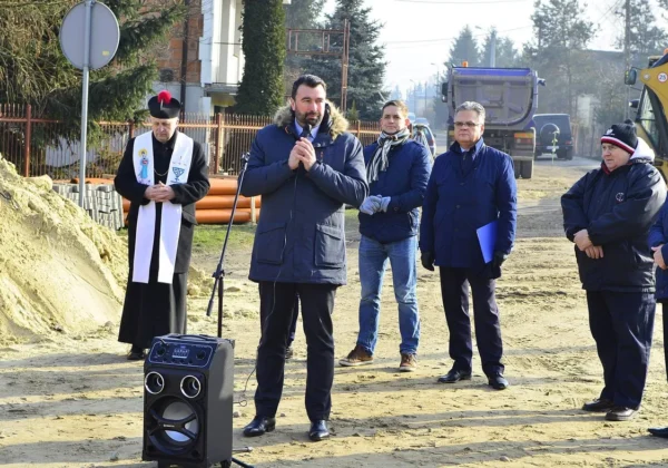 Podczas oficjalnego rozpoczęcia budowy kanalizacji w aglomeracji Bodzanów grupa mężczyzn w zimowych kurtkach stoi na placu budowy, jeden przemawia do mikrofonu, a w tle widać maszyny budowlane i rury.