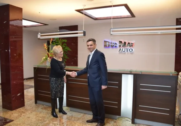 Kobieta i mężczyzna w formalnych strojach ściskają sobie ręce przy recepcji w biurze, symbolizując podpisanie porozumienia o współpracy partnerskiej.