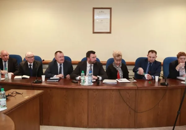 Grupa urzędników i samorządowców w garniturach siedzi przy długim stole w sali konferencyjnej urzędu powiatowego podczas oficjalnego spotkania.