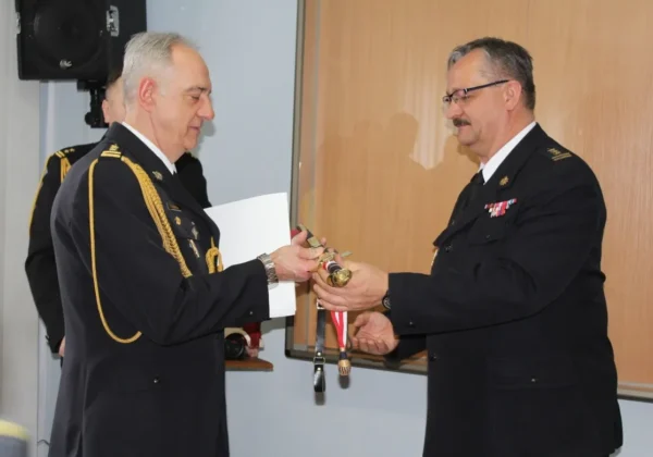 Dwóch strażaków w mundurach wymienia odznaczenia podczas ceremonii pożegnania zastępcy Komendanta Miejskiego PSP.