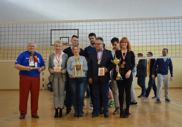 Grupa laureatów i organizatorów na boisku siatkarskim przed siatką, trzymająca trofea i medale podczas ceremonii wręczania nagród Ogólnopolskiego turnieju siatkówki o Puchar Starosty Płockiego.