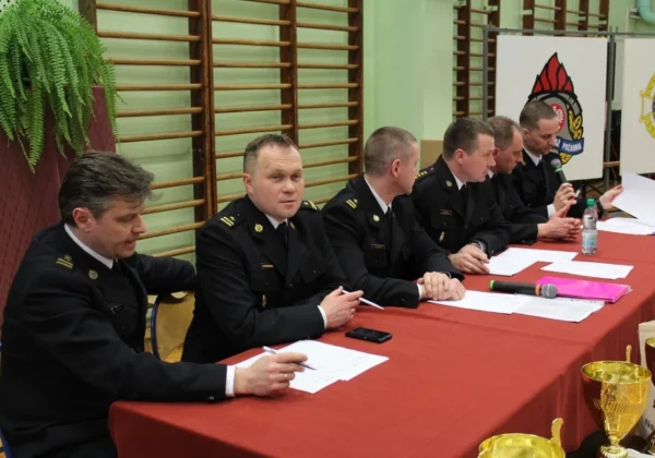 Grupa strażaków w mundurach siedzi za długim stołem z dokumentami i mikrofonami podczas XLI edycji Ogólnopolskiego Turnieju Wiedzy Pożarniczej „Młodzież zapobiega pożarom”.