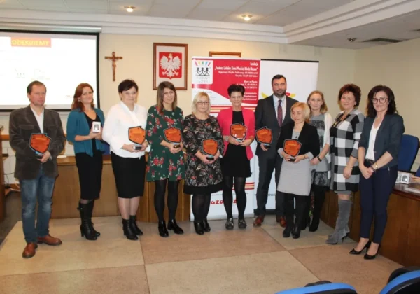 Grupa kilkunastu osób stoi w sali konferencyjnej, prezentując pomarańczowe odznaki nagród podczas warsztatów nt. grantów.