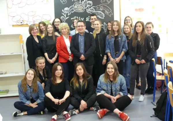 Grupa uczniów i nauczycieli na zajęciach języka niemieckiego w szkolnej klasie, stojąca i siedząca przed tablicą kredową z motywami roślinnymi i napisem „Deutsch hat Klasse”.