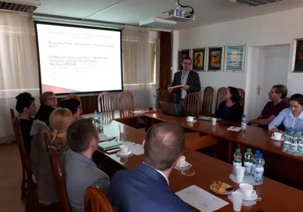 Prowadzący szkolenie kadrowe prezentuje slajdy na projektorze przed grupą uczestników siedzących przy stołach w sali konferencyjnej.