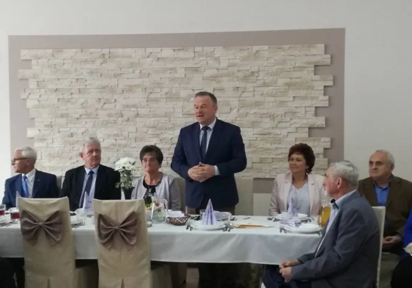 Mężczyzna w garniturze stoi i przemawia do zgromadzonych, siedzących przy stole podczas spotkania Powiatowej Sekcji Emerytów i Rencistów ZNP w Małej Wsi.