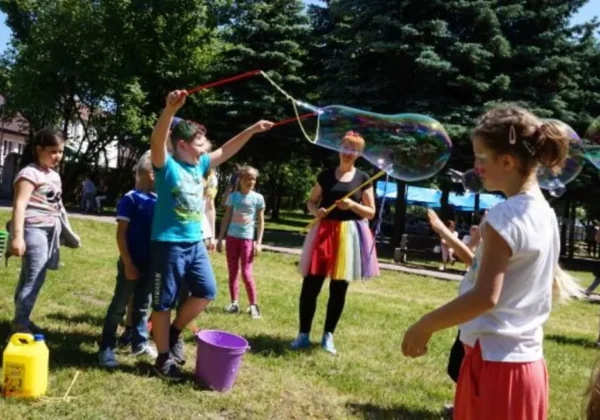 Dzieci na zielonym terenie podczas XII Letniego Pikniku Integracyjnego w Zespole Szkół Specjalnych w Goślicach puszczają bańki mydlane.