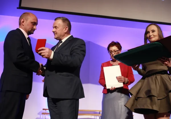 Na scenie podczas jubileuszu 25-lecia Szkoły Podstawowej Specjalnej nr 24 w Płocku dwóch mężczyzn wręcza nagrodę w czerwonym pudełku, a dwie kobiety trzymają teczki i dokumenty.