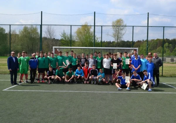 Grupowe zdjęcie chłopców piłkarzy z turnieju o Puchar Starosty Płockiego, stojących i klęczących przed bramką na boisku, z dyplomami i trofeami.