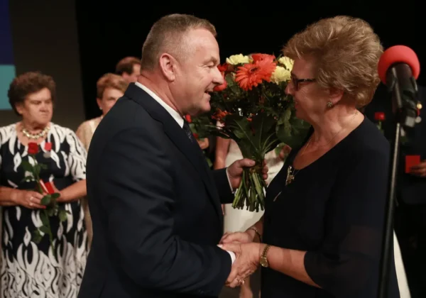 Mężczyzna w garniturze wręcza bukiet kwiatów starszej kobiecie podczas jubileuszu 50-lecia Polskiego Związku Emerytów, Rencistów i Inwalidów w Płocku.