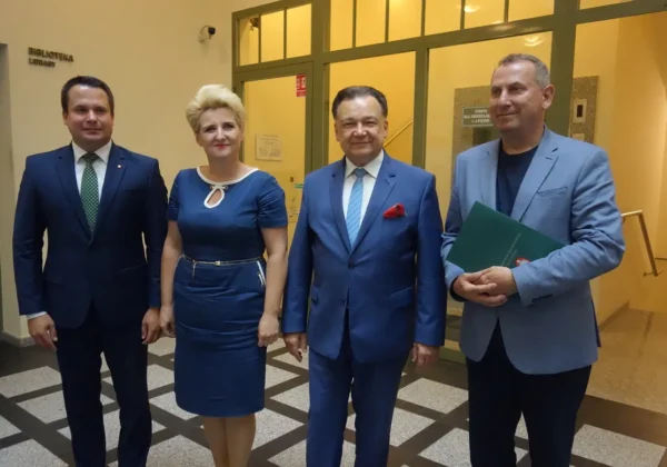 Czterech osób w eleganckich garniturach stoi razem w holu budynku, na tle wejścia, podczas oficjalnego spotkania związanego z remontami strażnic OSP na Mazowszu.