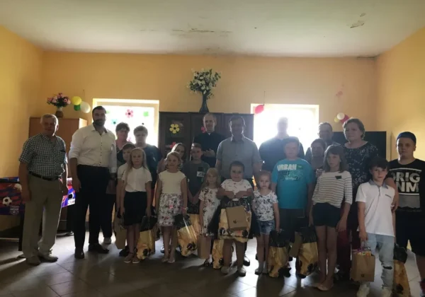 Dzieci i dorośli na Dniu Dziecka w Grodkowie stoją w sali udekorowanej balonikami i trzymają torby z upominkami.