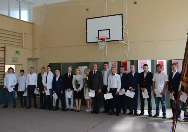 Grupa uczniów stojących w szeregu z dokumentami w dłoniach podczas uroczystości wręczenia świadectw w Zespole Szkół w Gąbinie, na sali gimnastycznej.