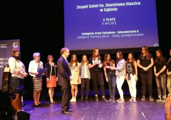 Na scenie stoi grupa uczniów i nauczycieli odbierających drugie miejsce w ogólnopolskim konkursie.