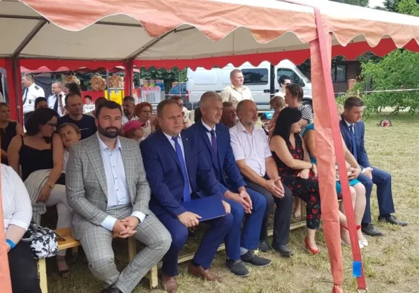 Grupa osób siedzi w rzędzie pod dużym pomarańczowym namiotem podczas VIII Dni Bulkowa i XVI festynu rodzinnego Stowarzyszenia „Nasza Przyszłość”.