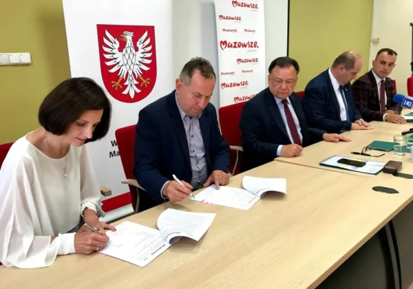 Grupa samorządowców z subregionu płockiego podpisuje umowy podczas konferencji MIAS 2018, przy stole z dokumentami, a w tle widać banery Mazowsza i godło Polski.