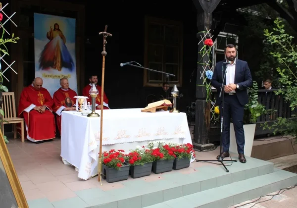 Uroczystość imienin Patrona DPS w Brwilnie Antoniego Juliana Nowowiejskiego: kapłani w czerwonych szatach liturgicznych siedzą przy ołtarzu, podczas gdy mężczyzna w garniturze przemawia przy mikrofonie.