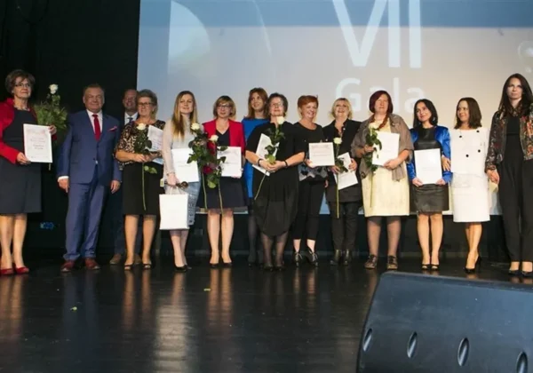 Grupa kobiet i jeden mężczyzna stoi na scenie podczas gali Wybory Kobiety Sukcesu Mazowsza 2018, wszyscy trzymają certyfikaty i kwiaty.