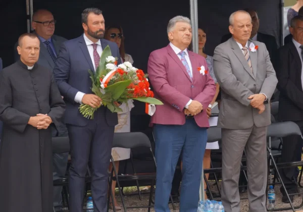 Grupa osób w garniturach i duchowny stoją na scenie podczas uroczystości upamiętniającej mieszkańców gminy Staroźreby; jeden z nich trzyma bukiet kwiatów.