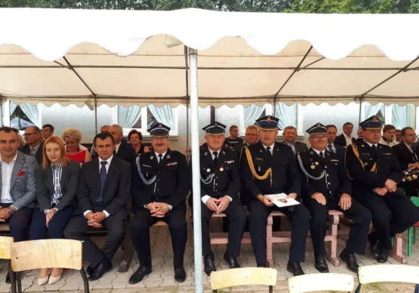 Grupa osób w mundurach strażackich i gości w garniturach siedzi pod białym namiotem podczas obchodów 100-lecia OSP Sobowo.