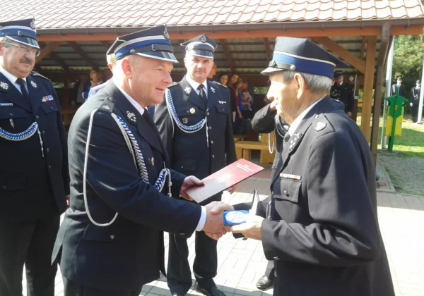Uroczystość jubileuszu 90-lecia OSP w Brwilnie — strażacy w mundurach składają gratulacje i wręczają odznaczenie podczas ceremonii.