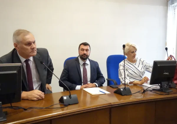 Trzech uczestników debaty siedzi przy długim, drewnianym stole konferencyjnym z mikrofonami i monitorami podczas spotkania o tematyce „Sukces pisany dotacją w ramach RPOWM 2014-2020”.