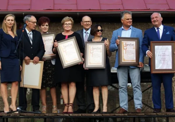 Grupa ośmiu osób stoi na scenie podczas obchodów 20-lecia Stowarzyszenia „Twoja Gmina” w Bodzanowie, trzymając w ramkach dyplomy i nagrody.