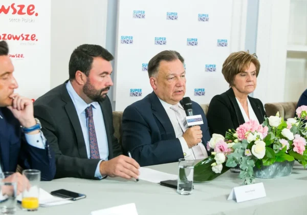 Panel dyskusyjny o transporcie autobusowym – czterech przedstawicieli siedzi przy stole z mikrofonem, notatkami i kwiatami, w tle banery z logotypem Super Biznes.