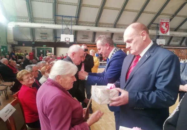 Uroczystość w sali gimnastycznej, podczas której wręczane są odznaczenia i upominki małżeństwom z gminy Łąck.