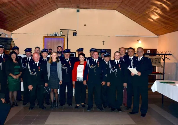 Grupa strażaków z Ochotniczej Straży Pożarnej w galowych mundurach wraz z kilkoma osobami cywilnymi stoi na sali podczas podsumowania działalności OSP w gminie Bulkowo, Mała Wieś i Wyszogród.