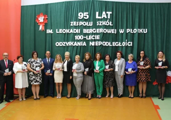 Grupa osób stojących na scenie przed zieloną kurtyną z napisem upamiętniającym 95 lat Zespołu Szkół i 100-lecie odzyskania niepodległości, trzymających drobne nagrody.